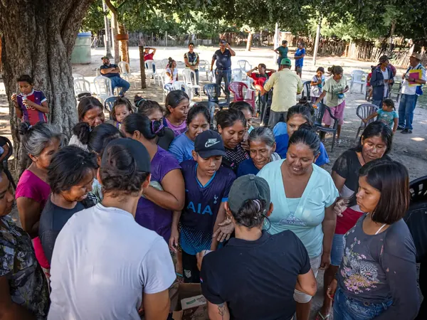 Women, young people and children crowd together at an outdoor Chaco Vivo community gathering, with more people seated beneath the trees behind them