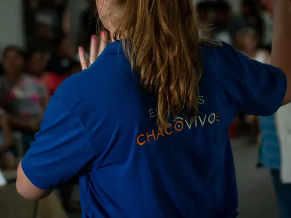Seen from behind, a team member in a blue Chaco Vivo shirt raises a hand while speaking to a seated audience