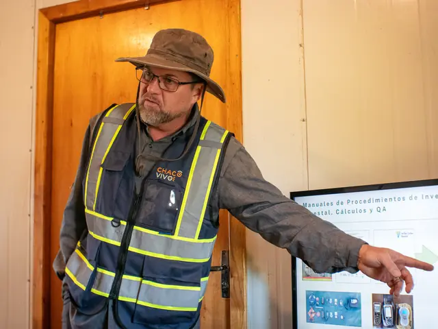 A team member in a Chaco Vivo high-visibility vest and hat points to a printed board headed “Manuales de Procedimientos de Inve…”, with “Cálculos y QA” visible on its title line