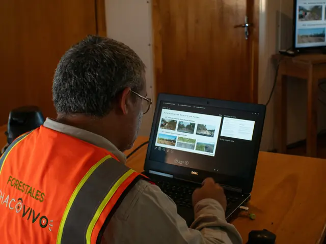 A man in an orange “Forestales Chaco Vivo” vest reviews a set of landscape photographs on a laptop at a desk